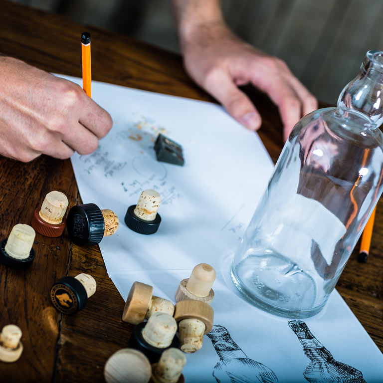 Korken, Skizzen und eine Flasche auf einem Holztisch: Ideenentwicklung bei den Idea Distillers.