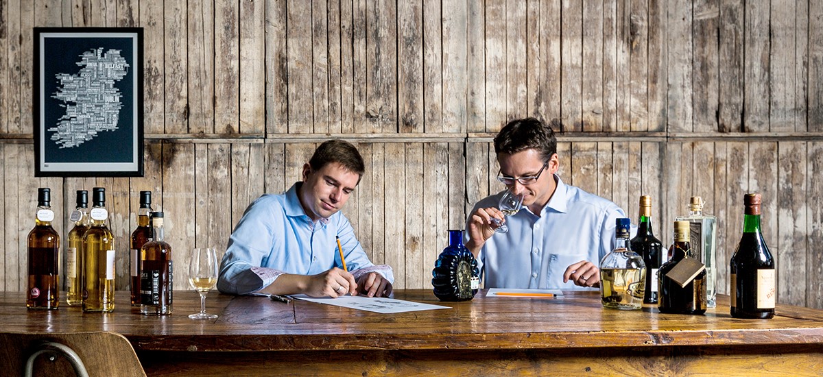 Die Idea Distillers Simon Weiß und Christian Schrade bei der Arbeit an einem Holztisch.